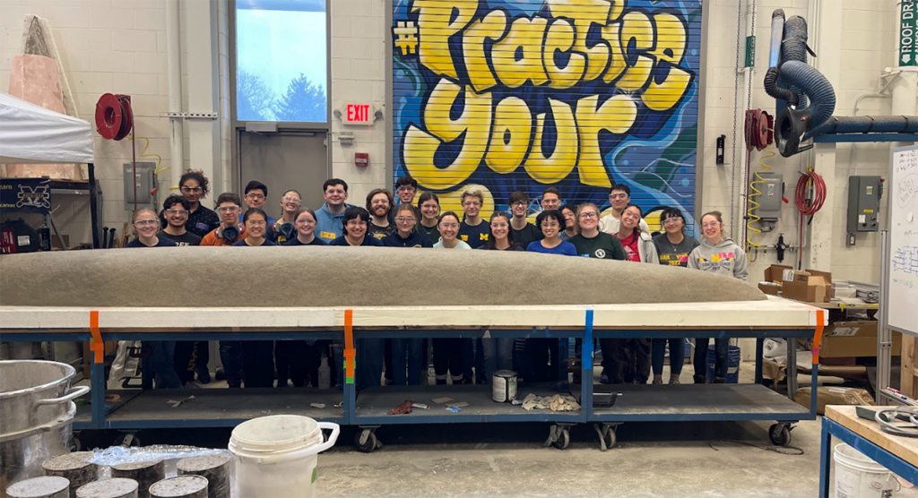 Concrete Canoe members standing behind the base of their canoe in the workshop.