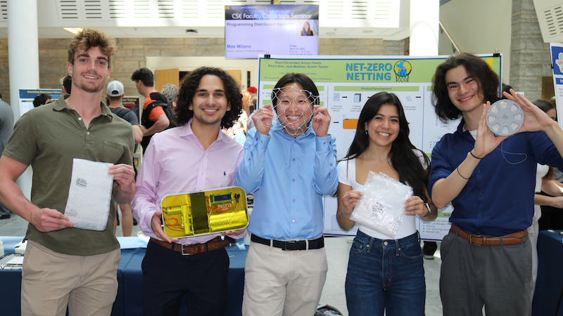 Photo of four undergraduate students posing for the photo in front of research posters.