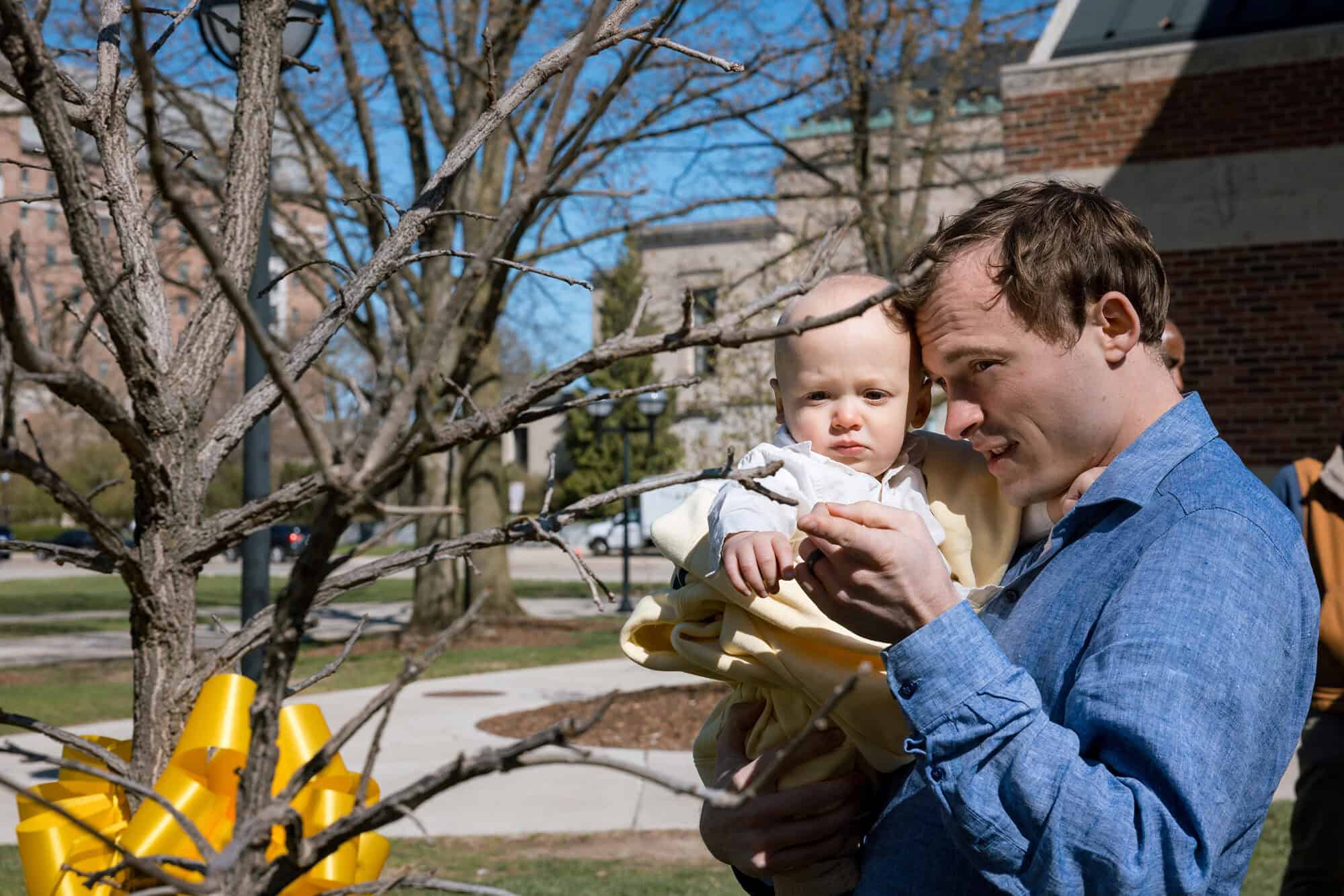 Chayce Griffith holds his 1-year-old son after helping plant the Tappan Oak sapling. (Connor Titsworth, Michigan Commons)